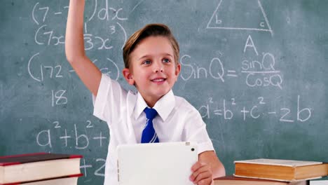 Schoolboy-raising-hand-while-using-digital-tablet-in-classroom