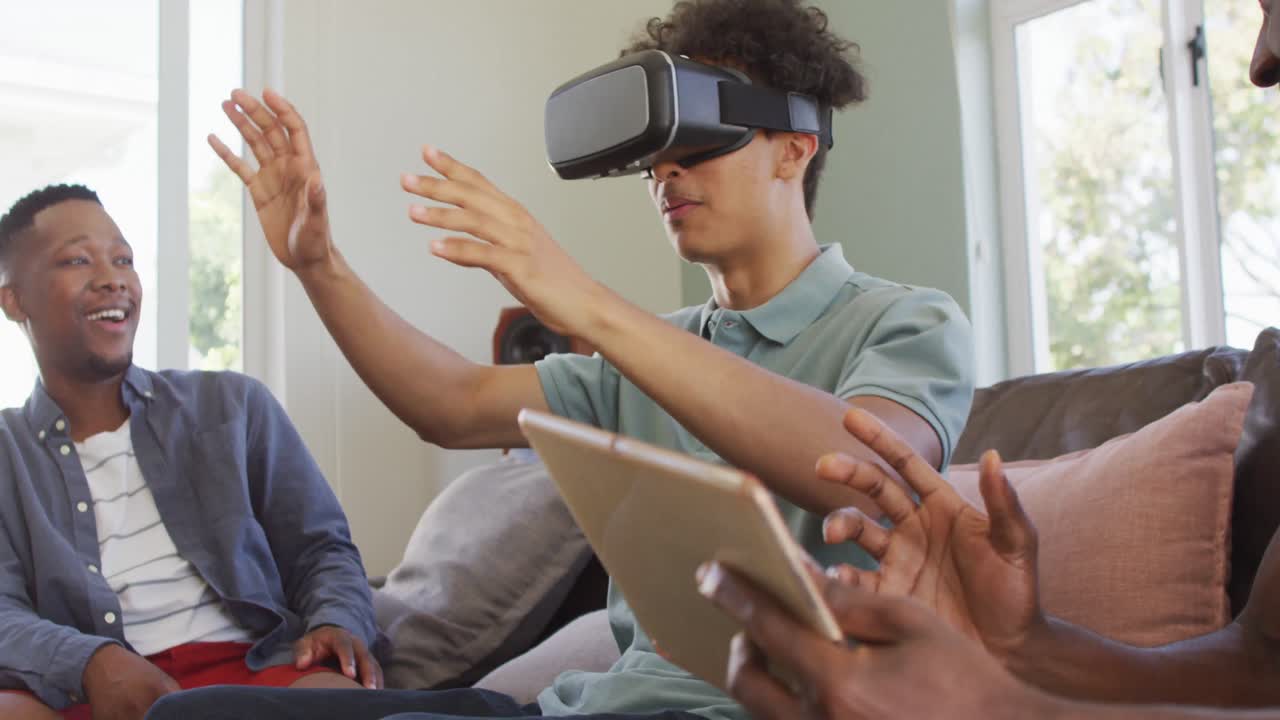 Happy diverse male friends using vr headset and talking in living room