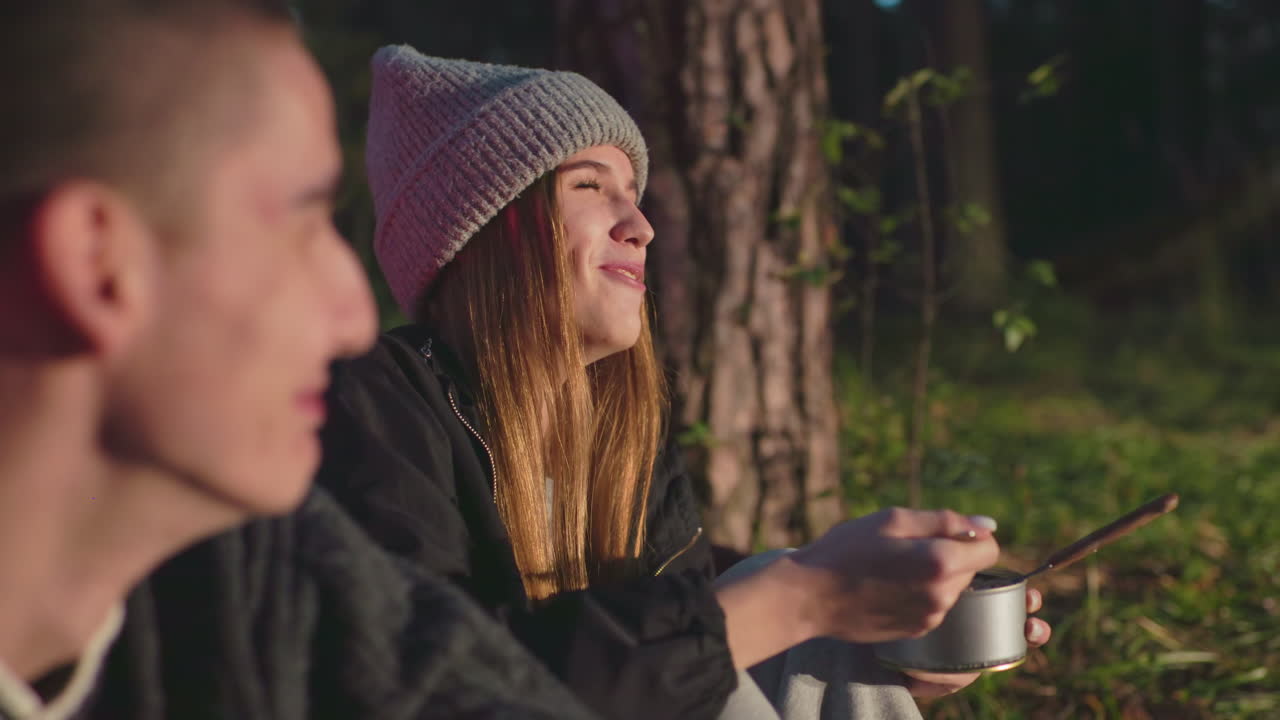 romantic moment between young couple laughing together outdoors woman eating food from can while man watches happy joyful sharing meal camping adventure nature love relationship
