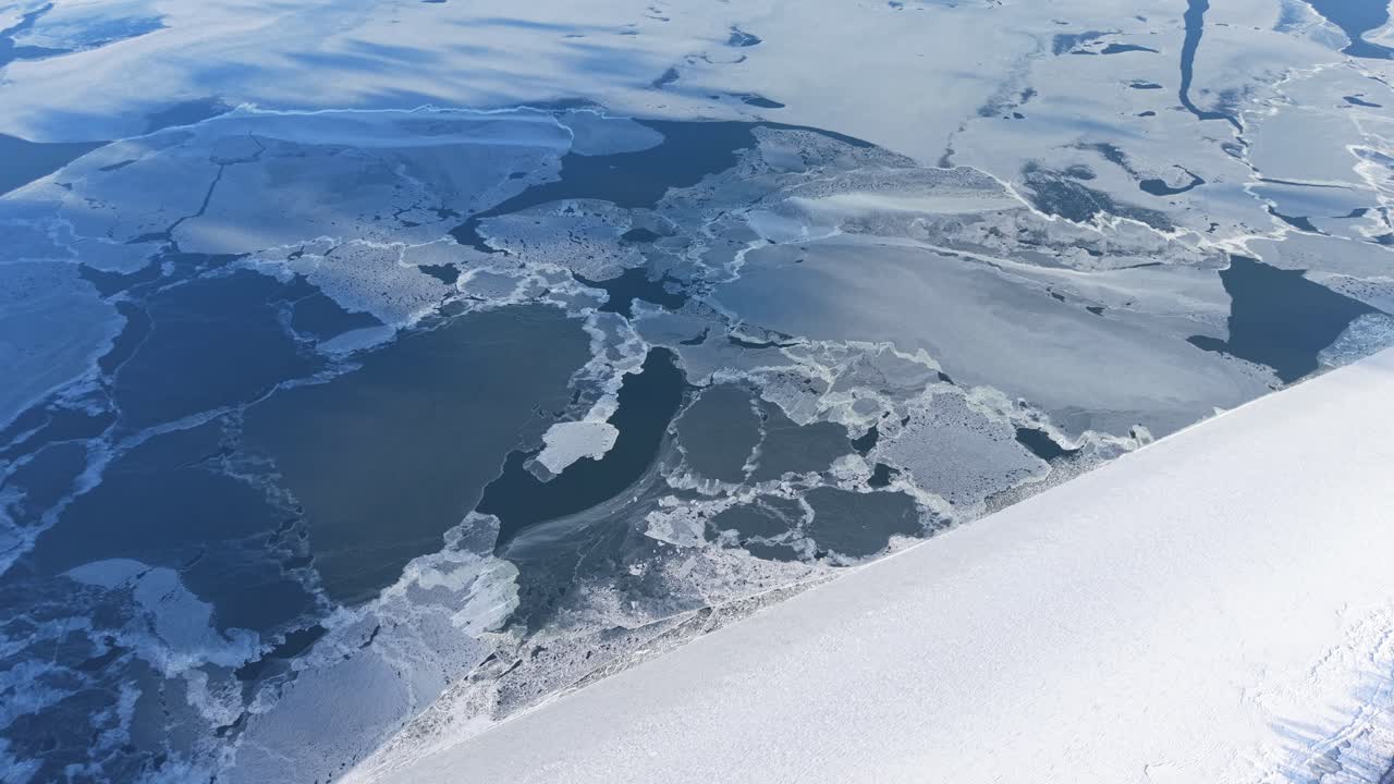 Formazioni di ghiaccio spezzate che galleggiano su un mare ghiacciato in condizioni invernali, rilassante sfondo aereo blu astratto.