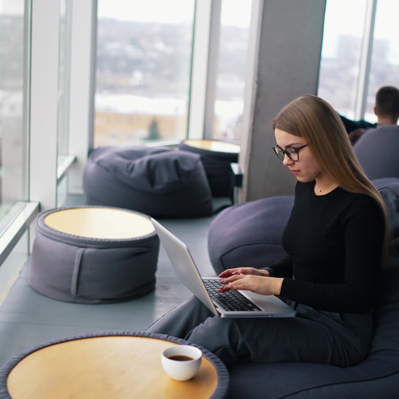 Female freelancer working on a laptop. Beautiful business woman sitting in a comfortable soft chair and typing on a wireless computer. Panoramic window view