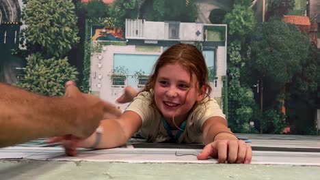 optical illusion of little girl clinging to wall of building pretending not to fall by grasping hand that pulls her up