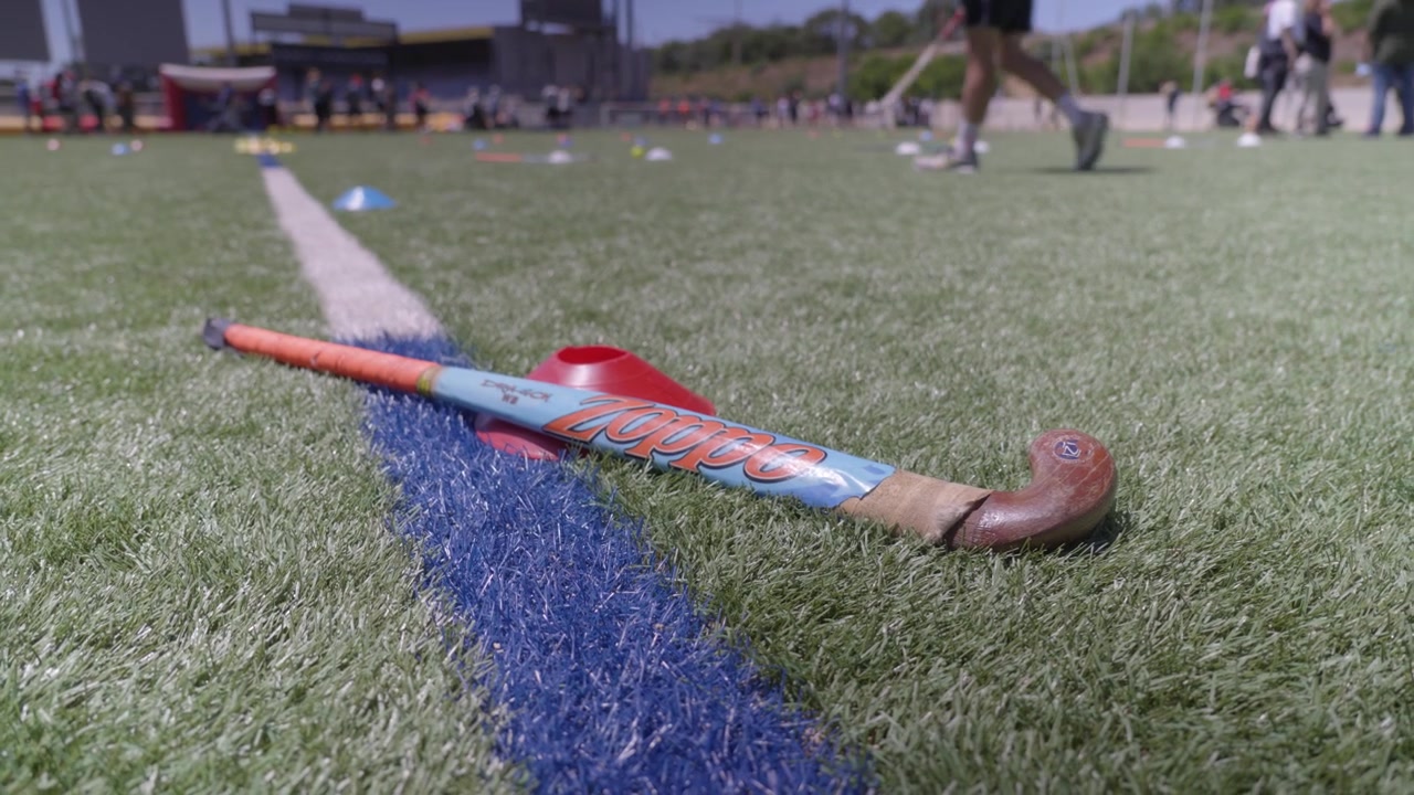 Bastone da hockey su prato e cono da allenamento su erba sintetica con giocatori sullo sfondo