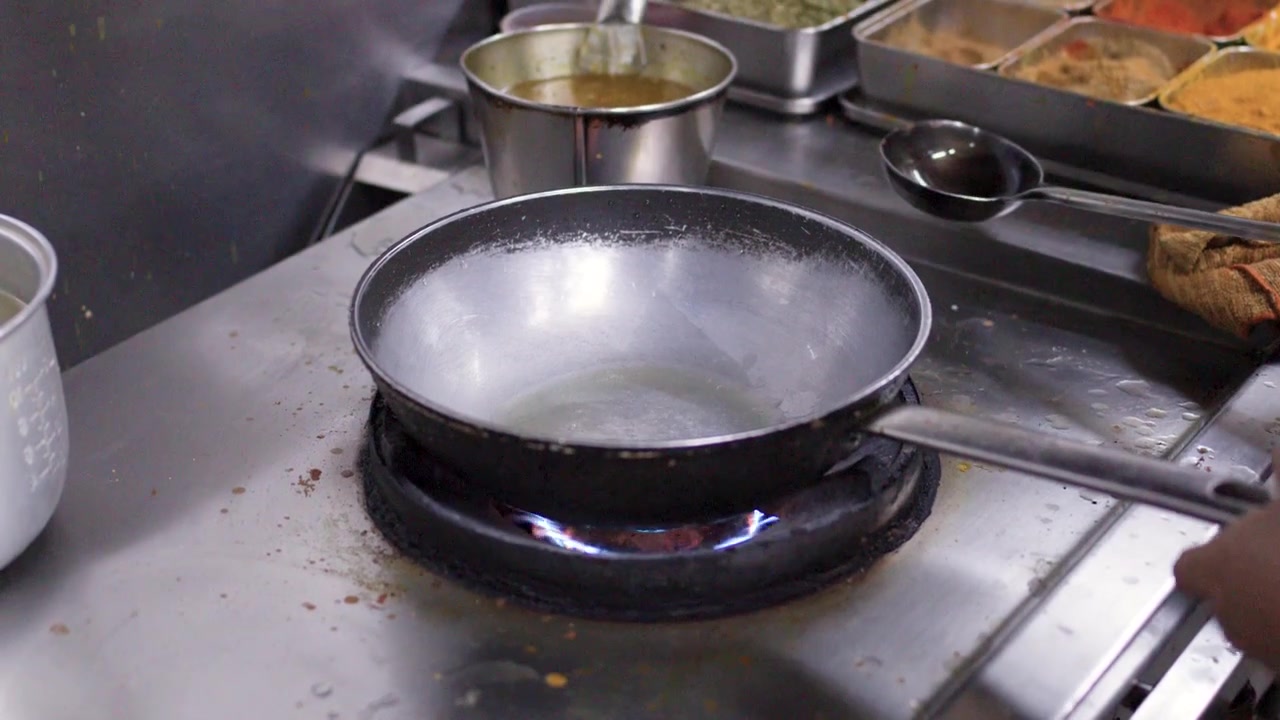 Professional chef prepares a stainless steel wok on high heat in a commercial kitchen.