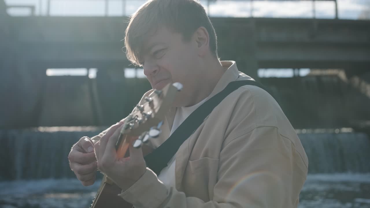 바위의 배경에 산의 강변에 앉아 기타를 연주하는 젊은이. 자유의 개념, 휴식 장소.