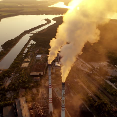 Smoking factory pipes at sunset. White smoke pours out of factory chimney in the air on the river background. Pollution, global warming concept. Aerial view.