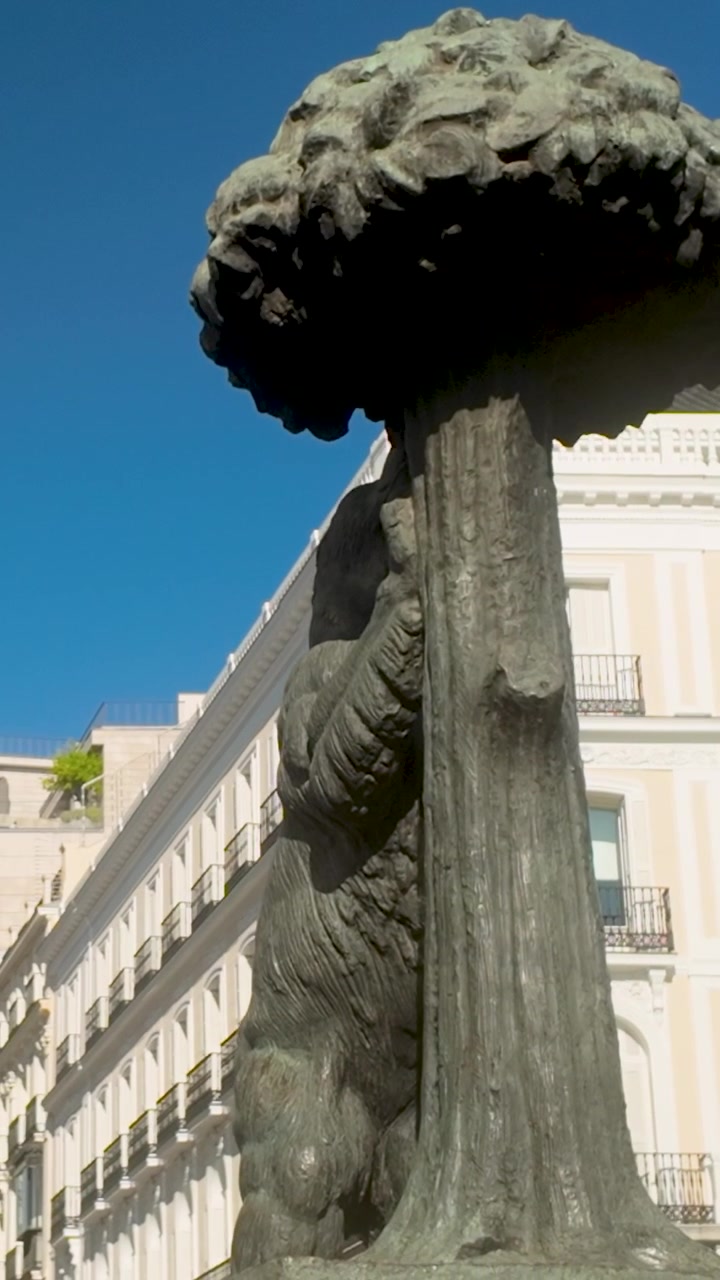 Primo piano dell'iconica statua "El Oso y el Madroño" a Puerta del Sol, Madrid, con architettura storica sotto un cielo azzurro limpido