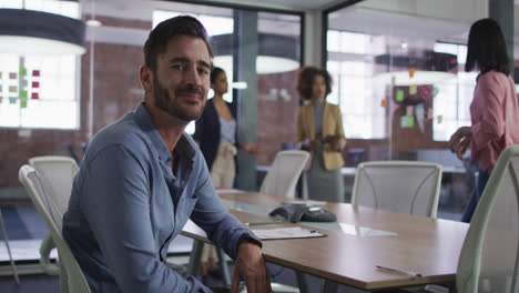 Caucasian-businessman-sitting-smiling-in-meeting-room-with-diverse-colleagues-in-background