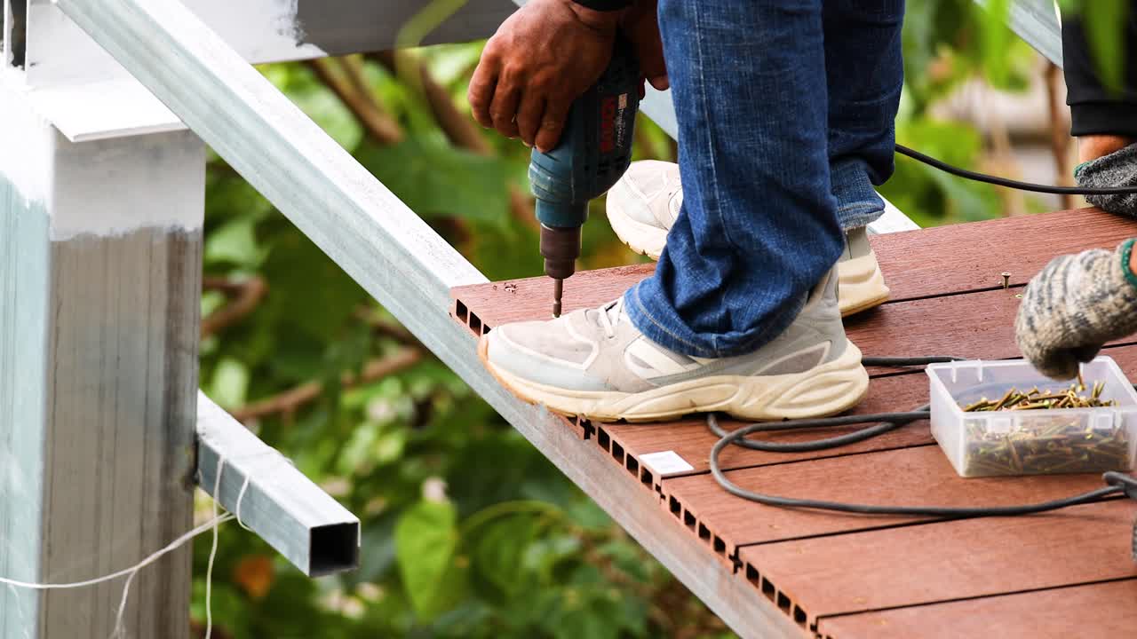 A carpenter uses a drilling machine on a rooftop in Phuket, Thailand. Bright daylight illuminates the construction scene