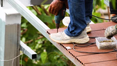 a carpenter uses a drilling machine on a rooftop in phuket, thailand. bright daylight illuminates the construction scene