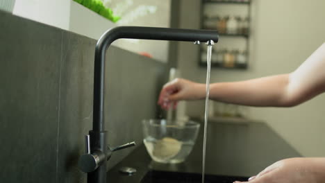 una ama de casa pelando patatas bajo agua corriente. preparando comida en su cocina