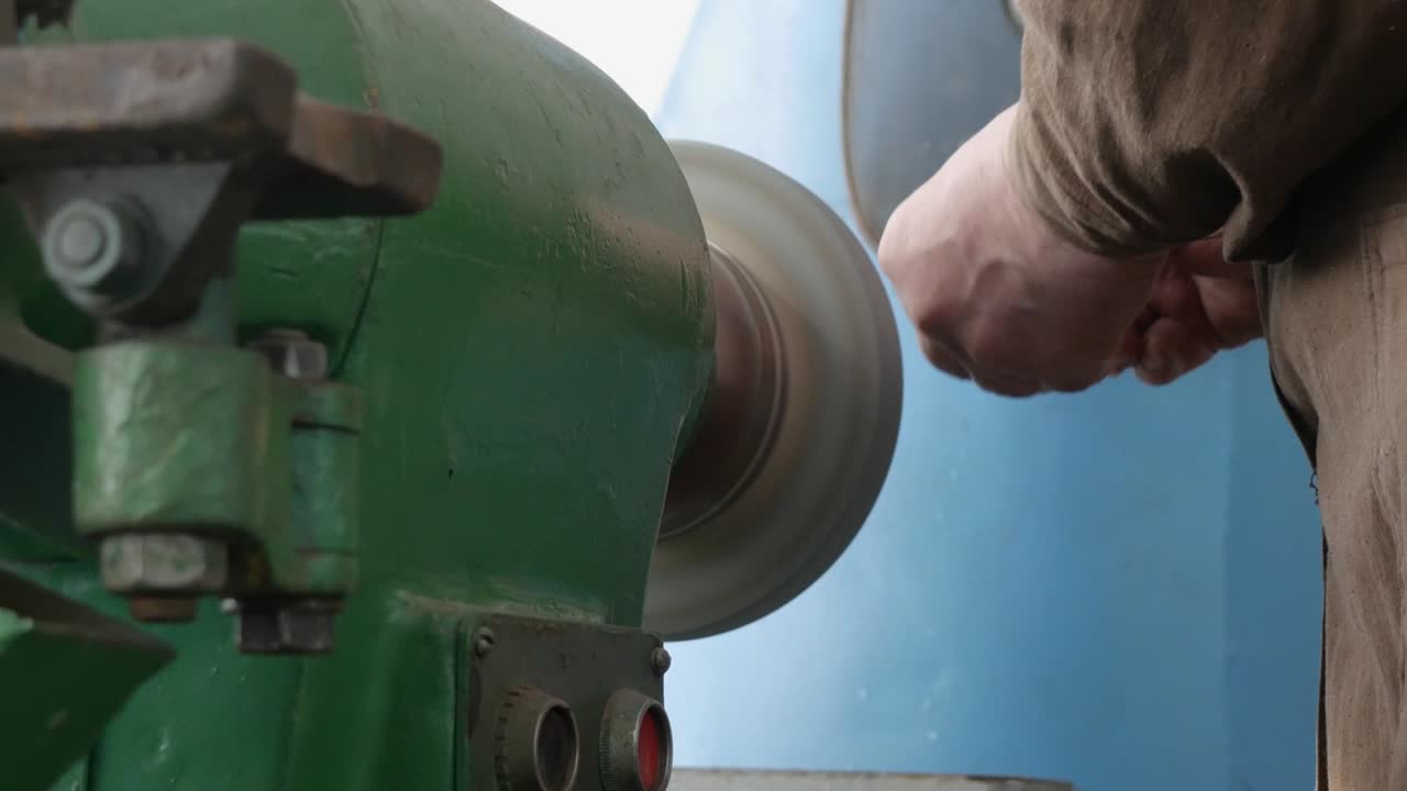 старые руки мастер шлифовать деталь на скамейке шлифовальной машины, грубая шлифовочная машина, крупный план. работа на пьедестальном шлифователе, производство предметов. финиш-шлифовальная металлическая часть на заводе
