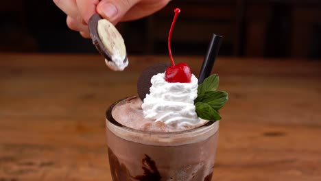 Detailed-close-up-of-malted-de-chocomenta,-with-caramel,-espresso-coffee-and-whipped-cream-with-cherry,-hand-taking-whipped-cream-with-a-chocolate-cookie-and-ice-cream