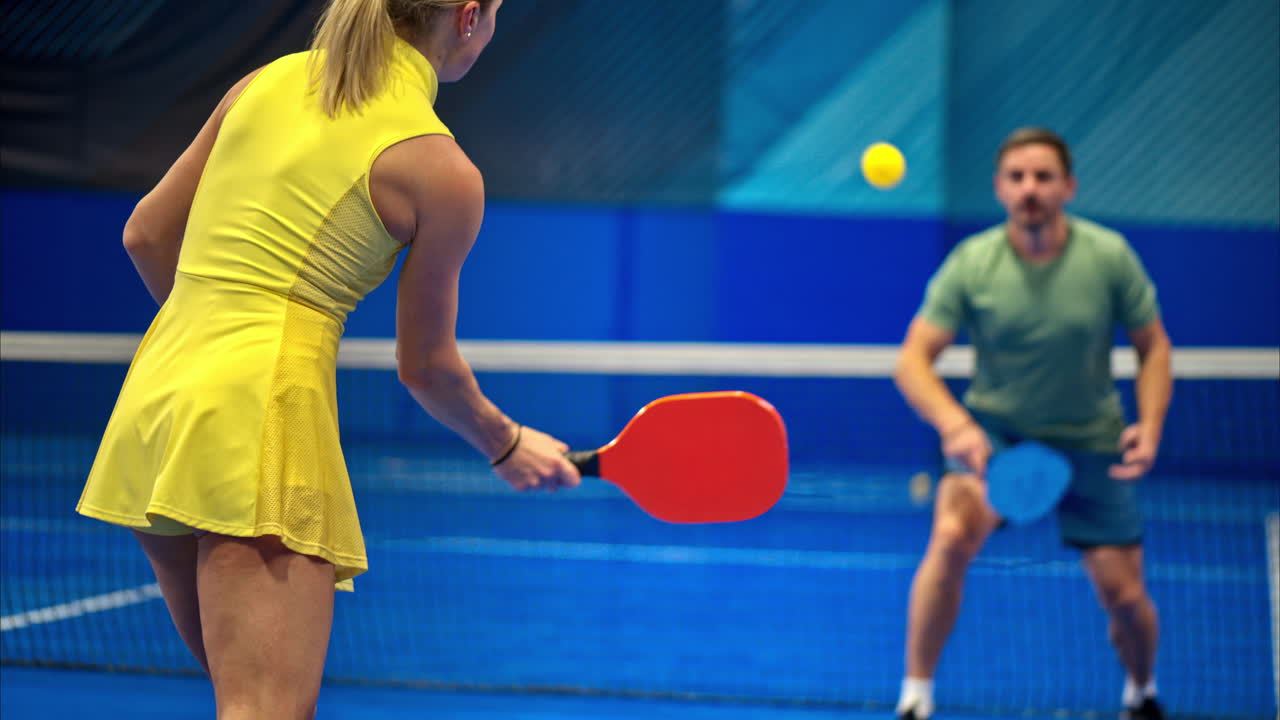 A man and a woman training to play pickleball on a blue, inside court