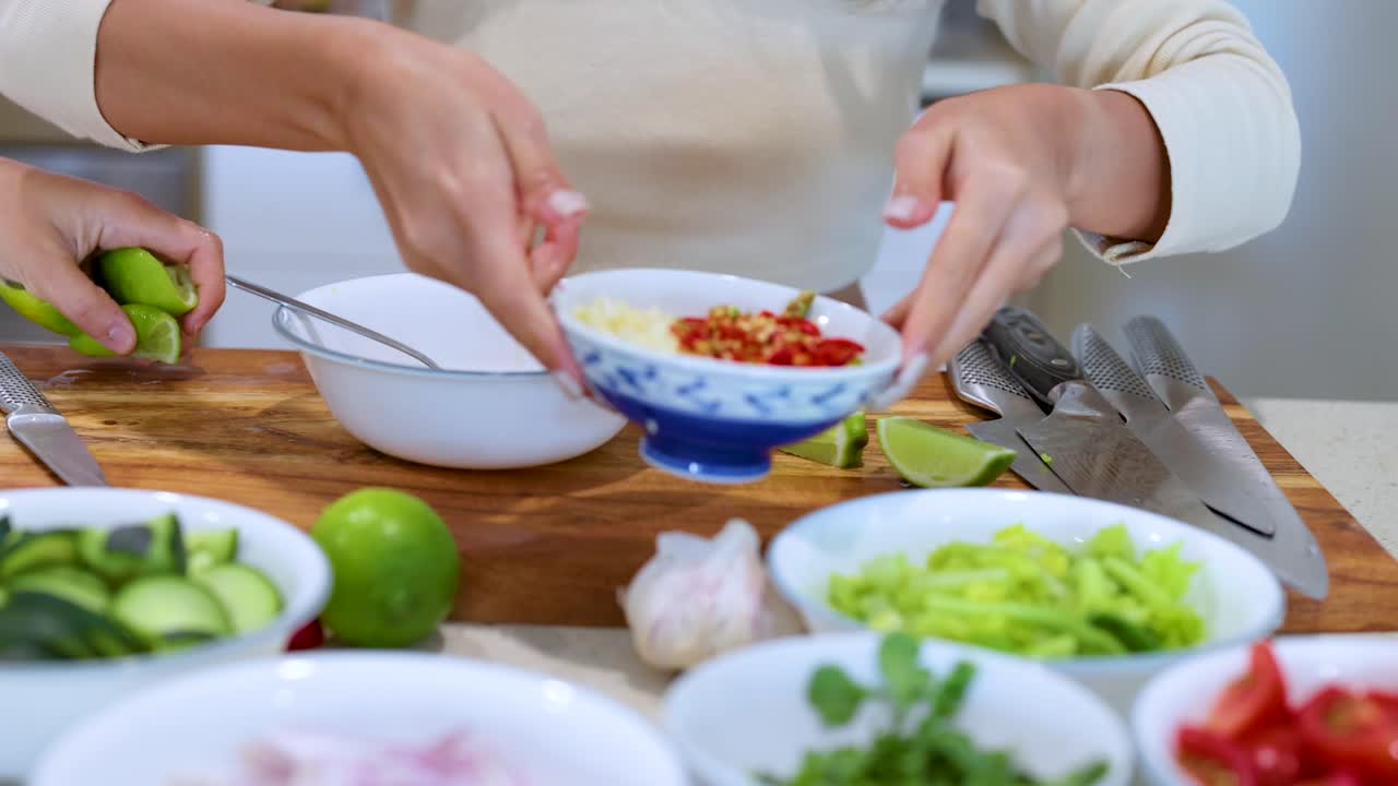 Hands arranging fresh vegetables and ingredients on a wooden board in a well-lit kitchen setting