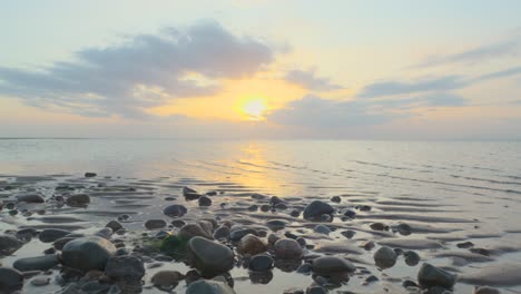 Glistening-pebbles-with-rise-up-showing-calm-sea-during-sunset-in-slow-motion-at-Fleetwood,-Lancashire,-UK