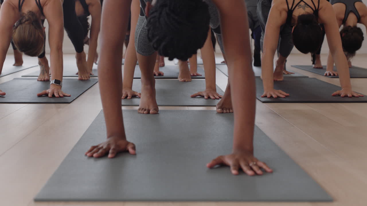 요가 수업 강사는 피트니스 스튜디오에서 건강한 라이프스타일 훈련 명상 연습을 즐기며 운동 매트 위에서 아래쪽을 향한 개 자세를 취하는 젊은 여성 그룹을 가르치고 있습니다.