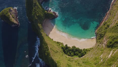 top-down drone view of the famous kelingking beach on nusa penida, bali, indonesia. the turquoise ocean, white sandy beach, and steep green cliffs create a stunning tropical landscape. shot in 4k.