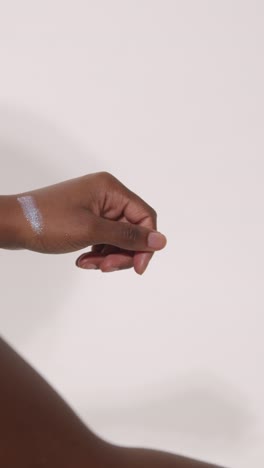 un primer plano de una mujer poniendo muestras de productos de maquillaje brillantes en su brazo