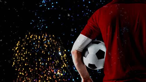 Animation-of-fireworks-over-back-view-of-caucasian-male-soccer-player-holding-ball