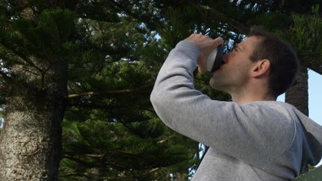 Young-caucasian-man-drinking-coffee-sitting-on-a-park-bench-in-Auckland,-New-Zealand