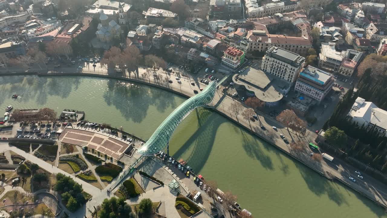 Aerial view of the Bridge of Peace and surrounding riverfront area in Tbilisi. The photo captures daily urban life and architectural contrast between old and new city parts