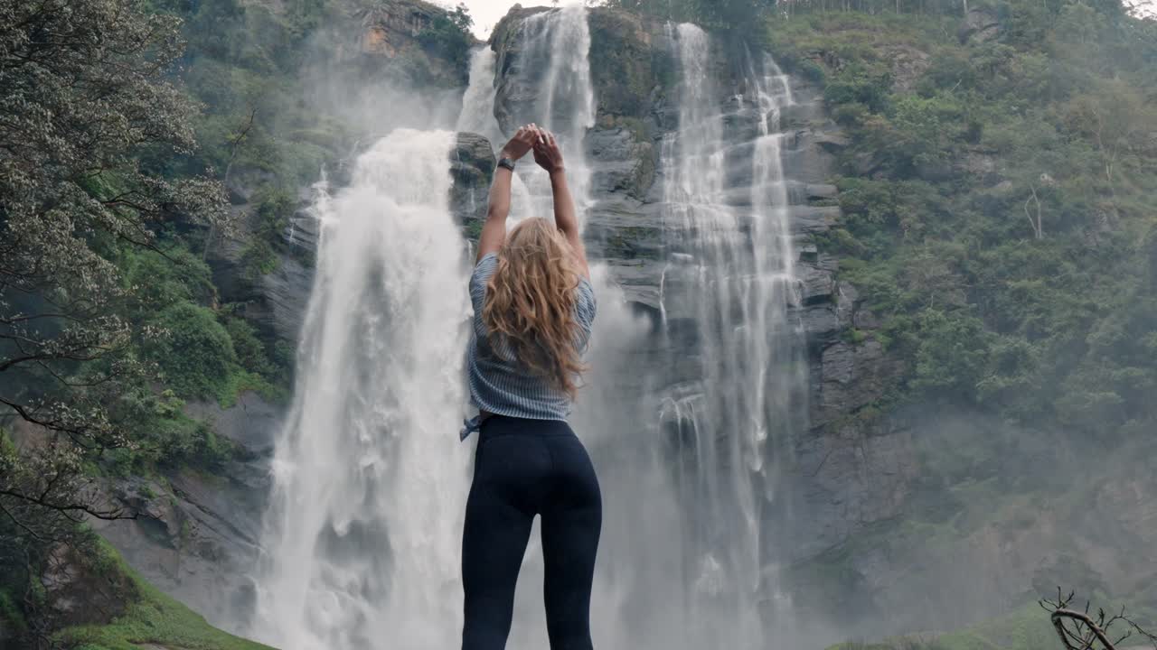 A woman stands in awe before the roaring Bomburu Ella Waterfalls, surrounded by mist, jungle, and rocky cliffs in the lush highlands of Nuwara Eliya, Sri Lanka.