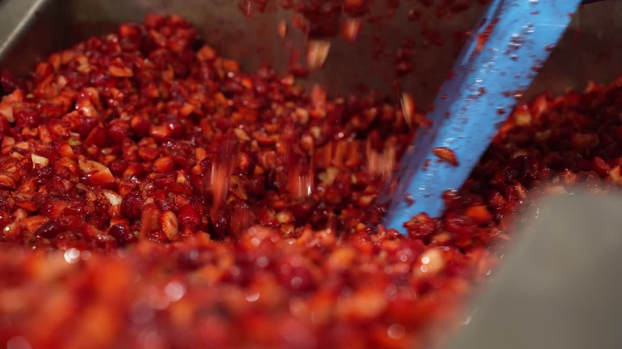 Cut strawberries in production being scooped and stirred