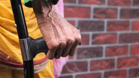 elderly woman's hand gripping crutches against brick wall