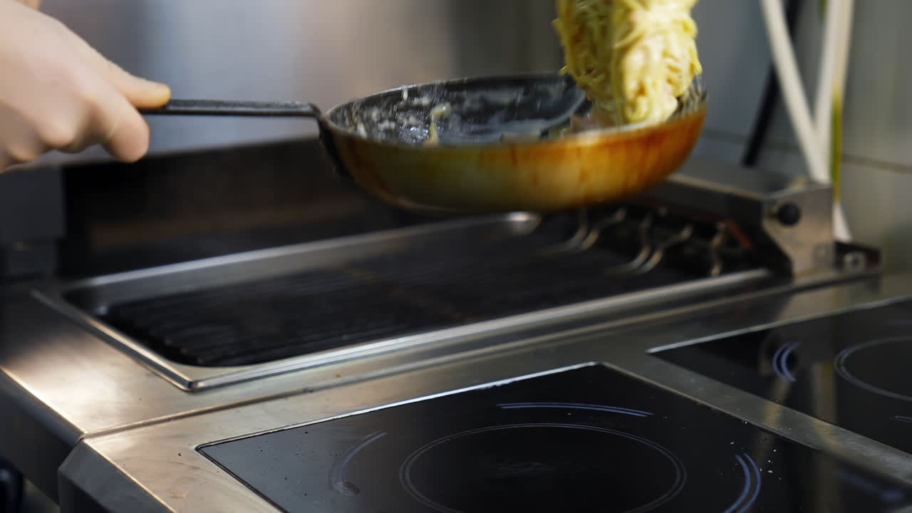 Cooking meals in a restaurant. Chef is cooking dish in a frying pan and flipping throwing it. Cooking the spaghetti in white sauce in the frying pan. Close-up.