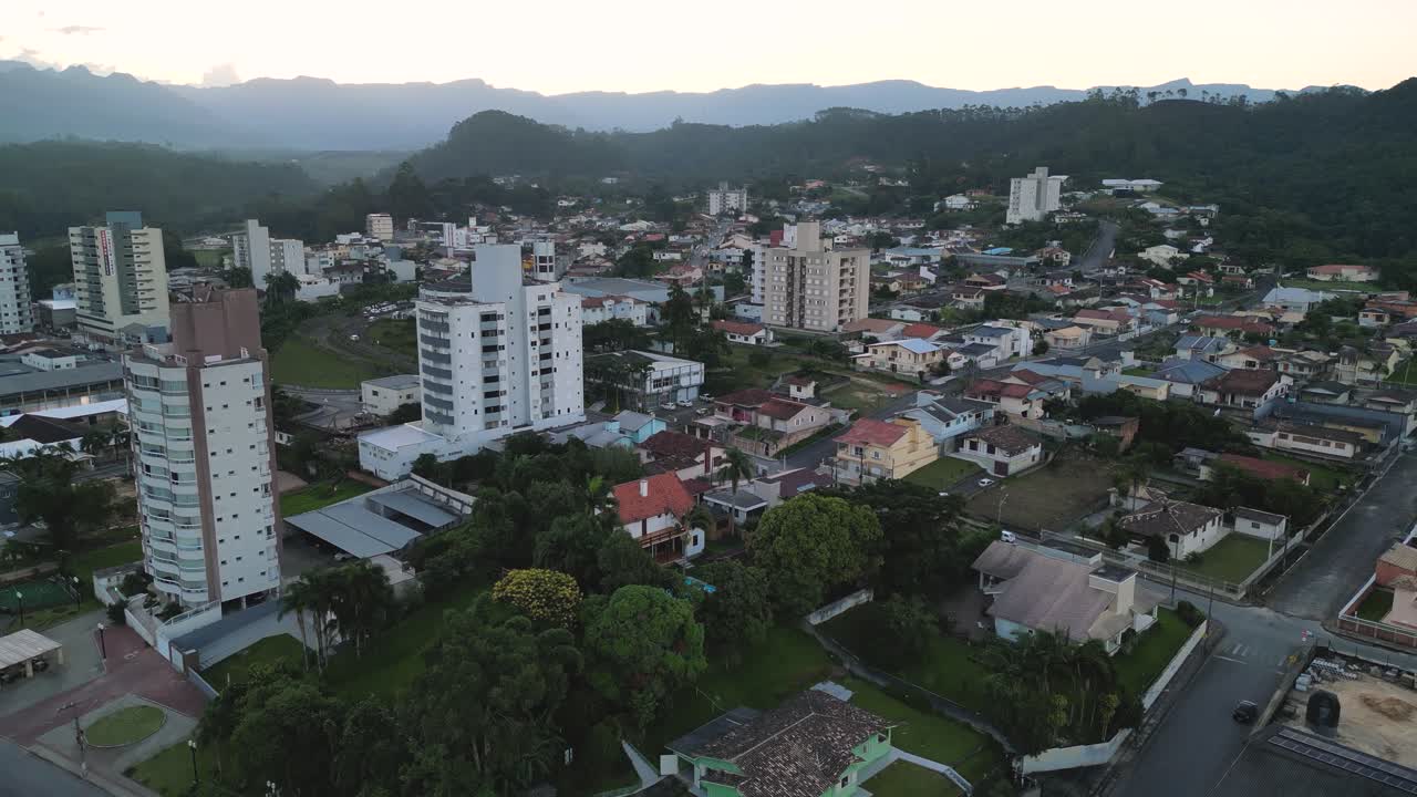 Lauro Muller's urban core at dawn, focusing on several modern apartment and office towers contrasting with the surrounding low-rise residential areas and green mountain backdrop