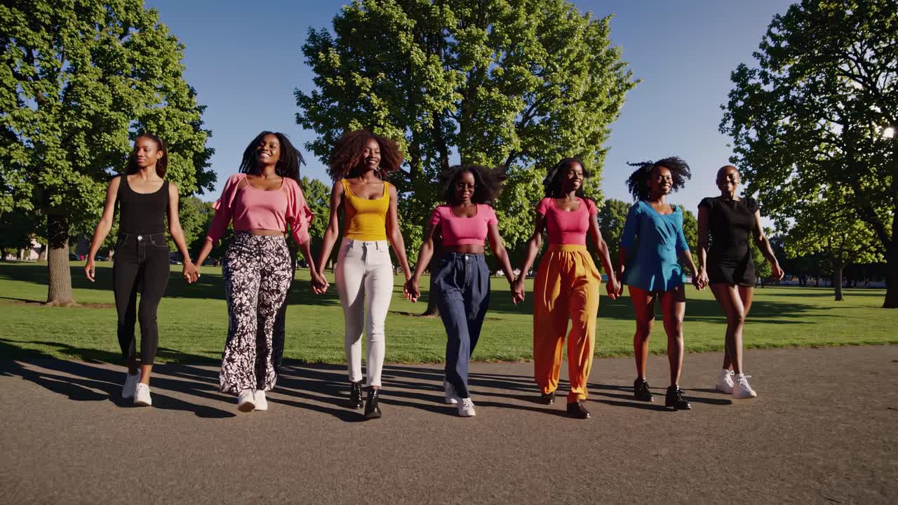 A low-angle video captures a group of women walking hand in hand in a park, showcasing unity