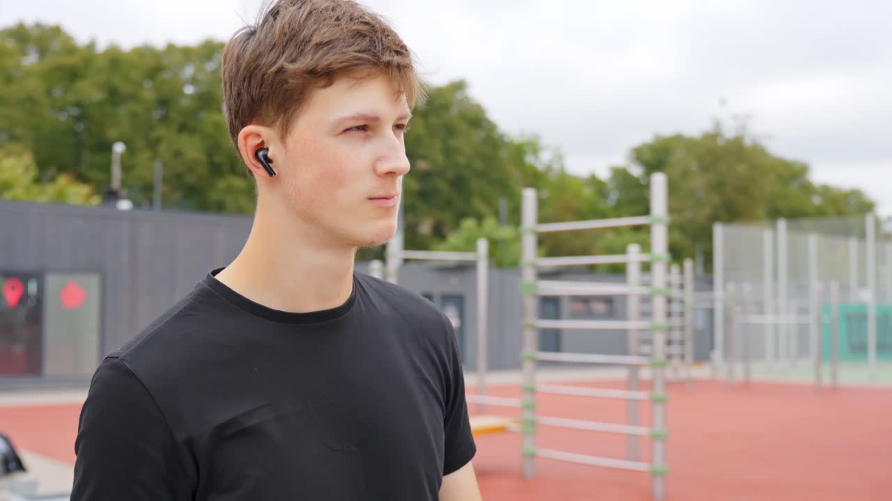 Active male in sports park listens to music through earpads, nodding head to rhythm