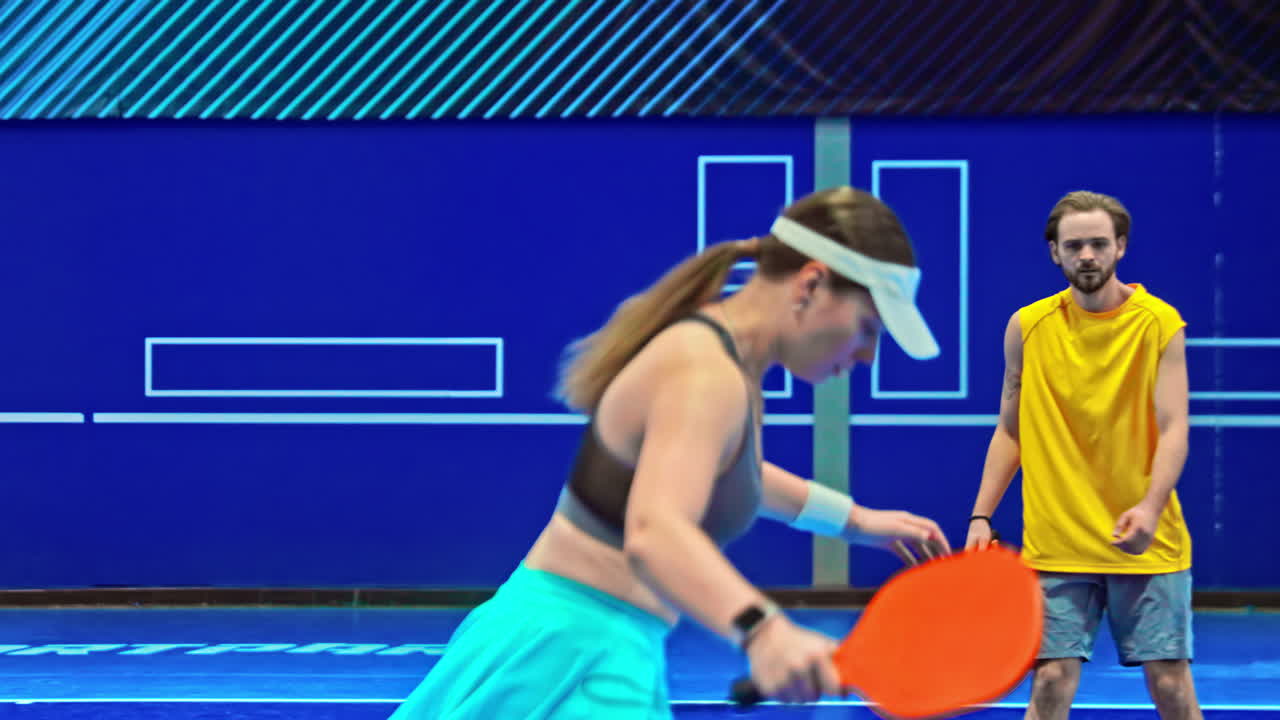 A man and a woman playing pickleball on a blue, inside court