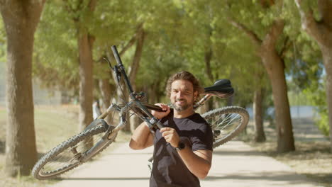 front view of cheerful man standing on alley with bike in hands