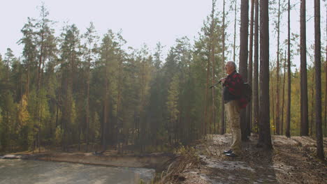 inspired man is standing in forest and admiring nature enjoying warm autumn weather holding backpack and rod
