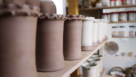 Close-Up-Of-Male-Potter-Taking-Clay-Vase-From-Shelf-To-Glaze-In-Ceramics-Studio