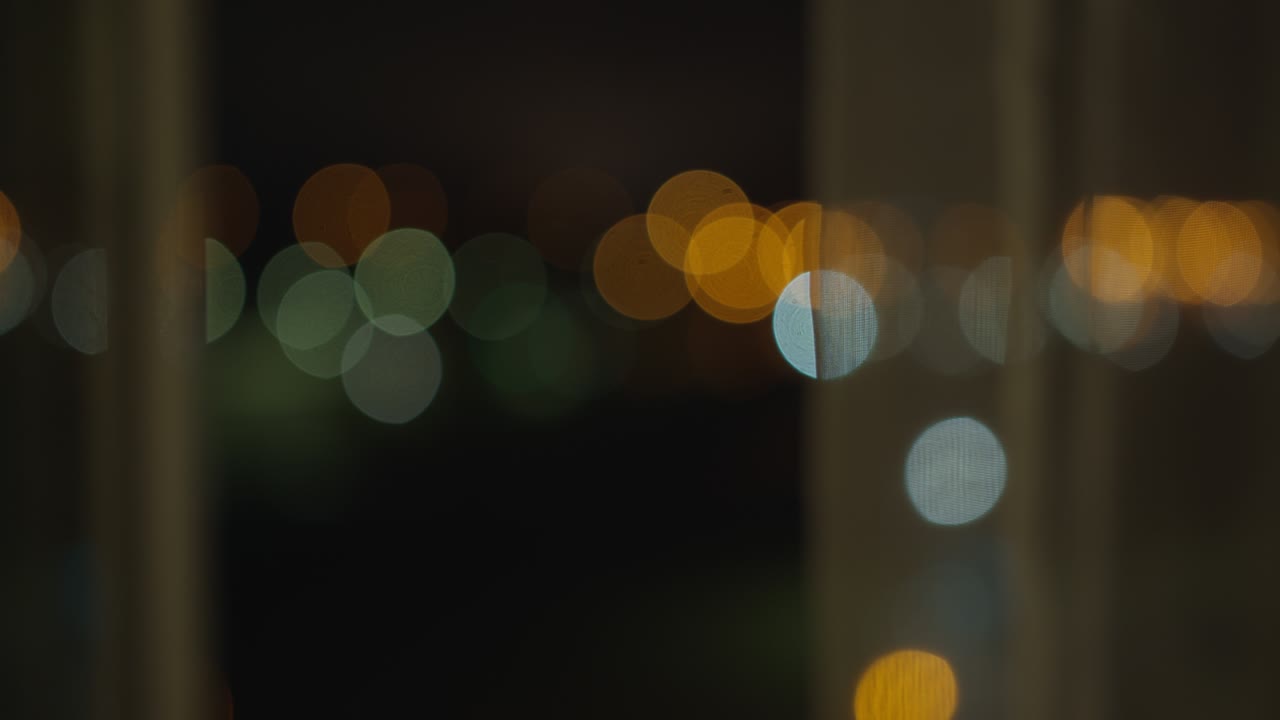 Open window at night, blurry city lights behind tulle