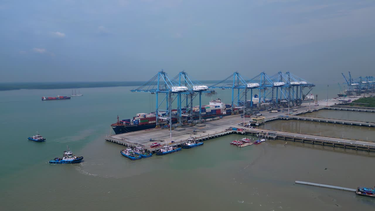 Container ship docked at a busy commercial port, cranes loading cargo containers. Global logistics and maritime trade infrastructure. Smooth aerial view wide orbit panorama overview drone
