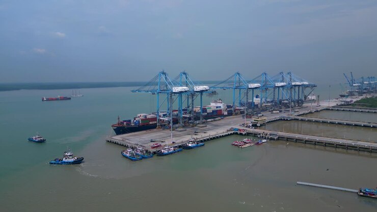 Container ship docked at a busy commercial port, cranes loading cargo containers. Global logistics and maritime trade infrastructure. Smooth aerial view wide orbit panorama overview drone