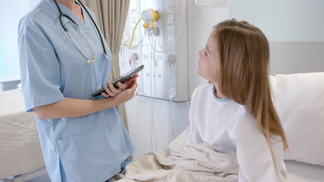 caucasian female doctor with tablet talking with girl patient in hospital bed, slow motion