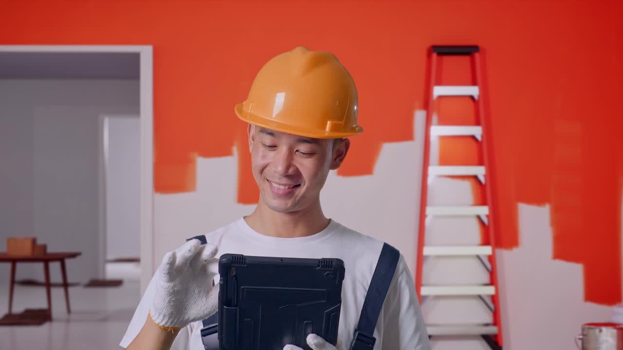 trabajador de la construcción inspeccionando el trabajo usando una tableta digital en una habitación con una pared recién pintada