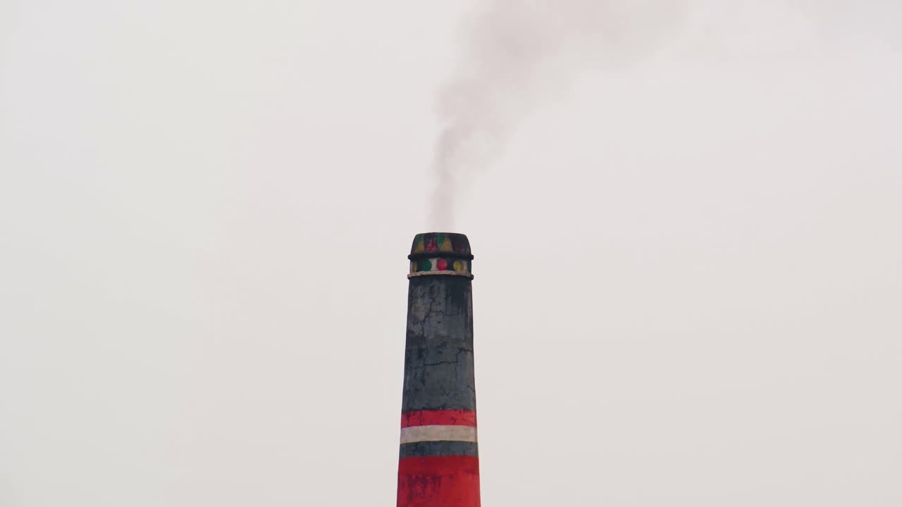 vista media de la chimenea de la fábrica de campo de ladrillo emitiendo pequeño humo negro