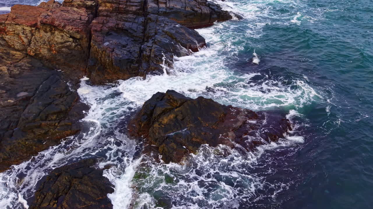Waves crashing against rugged rocks at the coastline during sunset, creating a breathtaking view of nature's power and beauty in the evening light