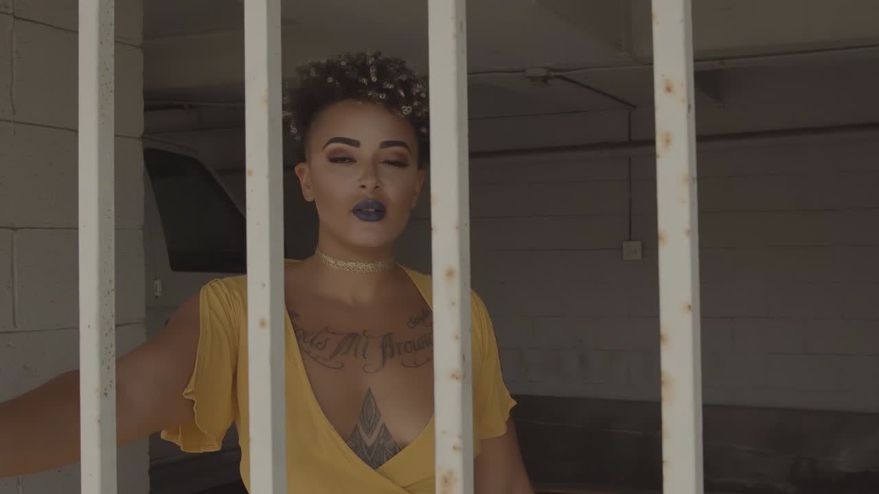 Young woman wearing a yellow dress walking towards while being behind rusty bars