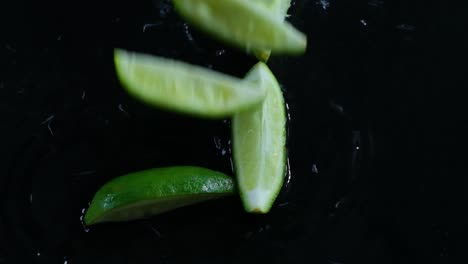 Lime-slices-fall-on-wet-black-surface,-reverse-studio-shot