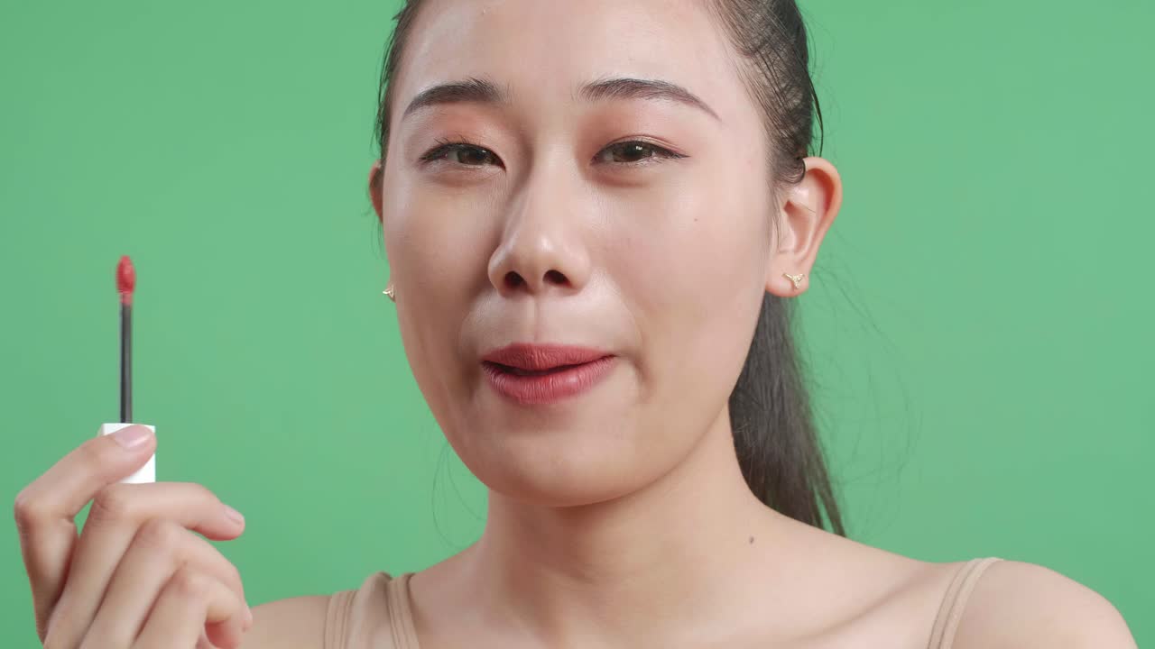 스튜디오의 녹색 화면 배경에서 미소 짓는 동안 립스틱을 적용하는 아시아 여성의 클로즈업