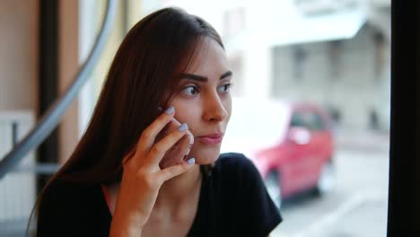 Close-Up-view-of-attractive-young-woman-talking-on-the-phone-in-a-cafe-sitting-by-the-window-in-the-cafe