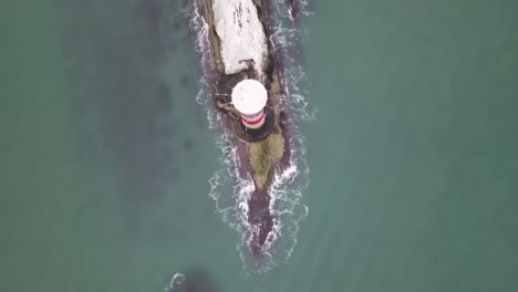 Vuelo-Aéreo-De-Drones-Que-Ofrece-Una-Vista-De-Pájaro-Del-Faro-Rojo-Y-Blanco-En-Las-Agujas-De-La-Isla-De-Wight-Que-Muestra-Olas-Rompiendo-Contra-Las-Rocas-De-Abajo