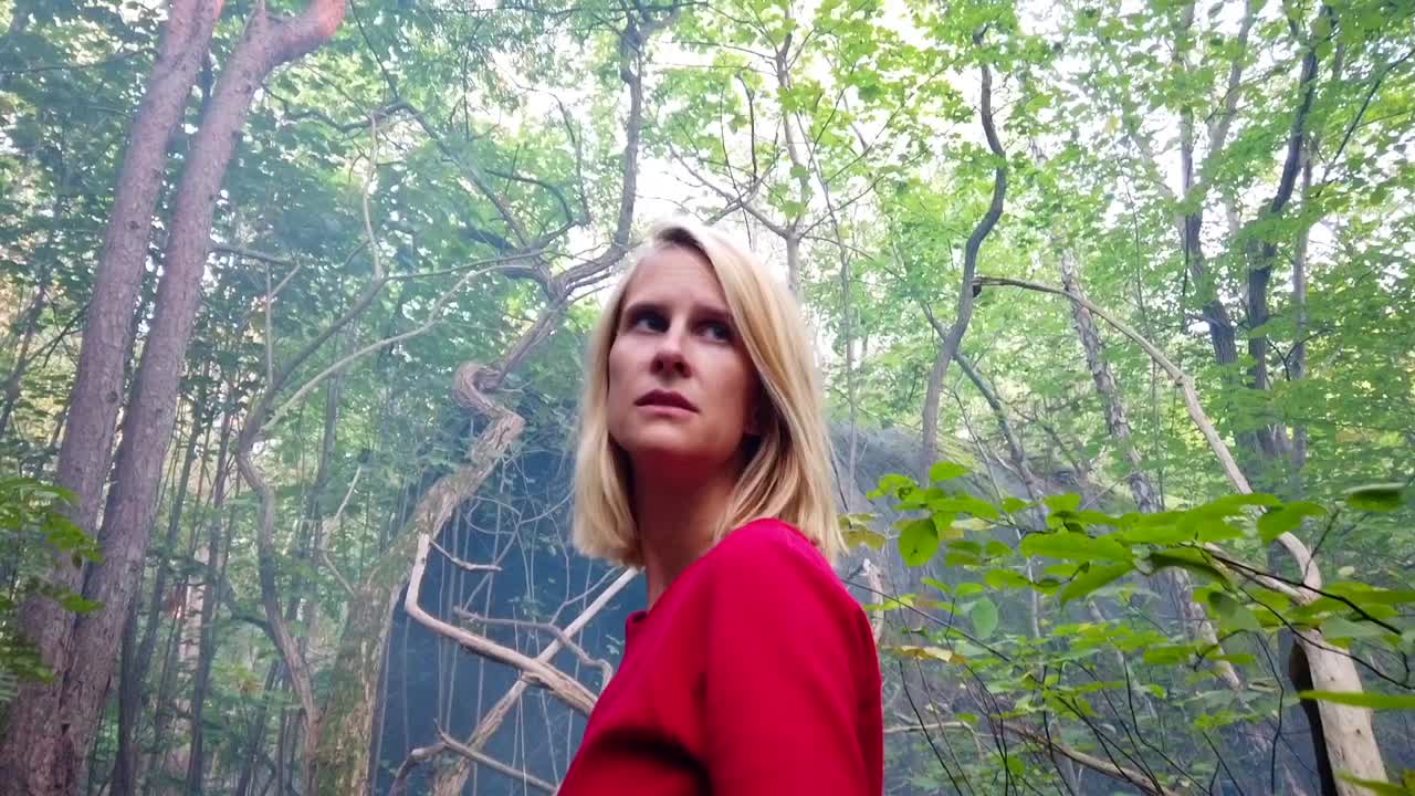 Gorgeous slow motion cinematic shot of a lonely girl in a red dress sitting on a tree with a disco ball looks scared in the wood. Foto video shoot on lost places in nature 1080, 24p by Philipp Marnitz